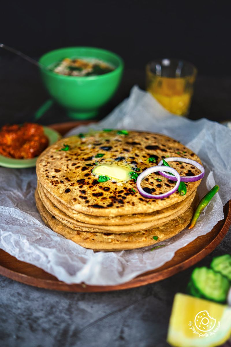 -photo of a stack of paneer paratha flatbreads with onions and cucumbers on a plate