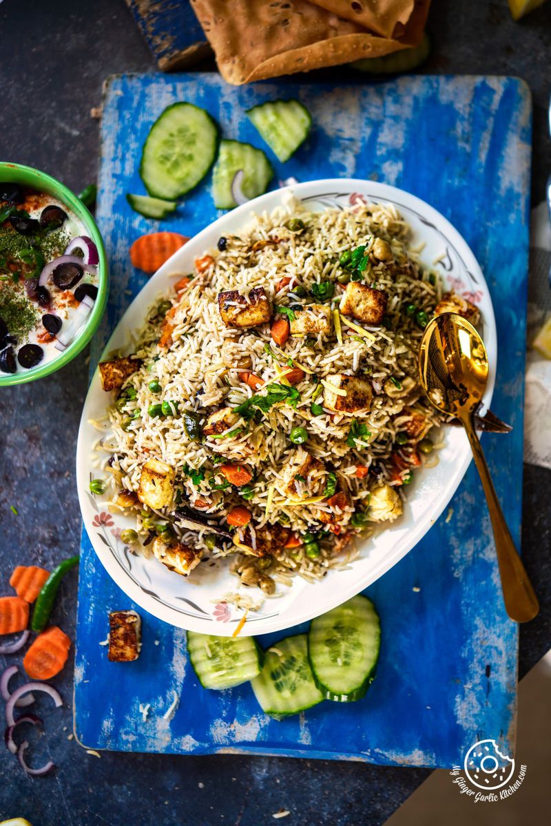 overhead closeup shot of paneer rice with raita and cucumber slices on the side