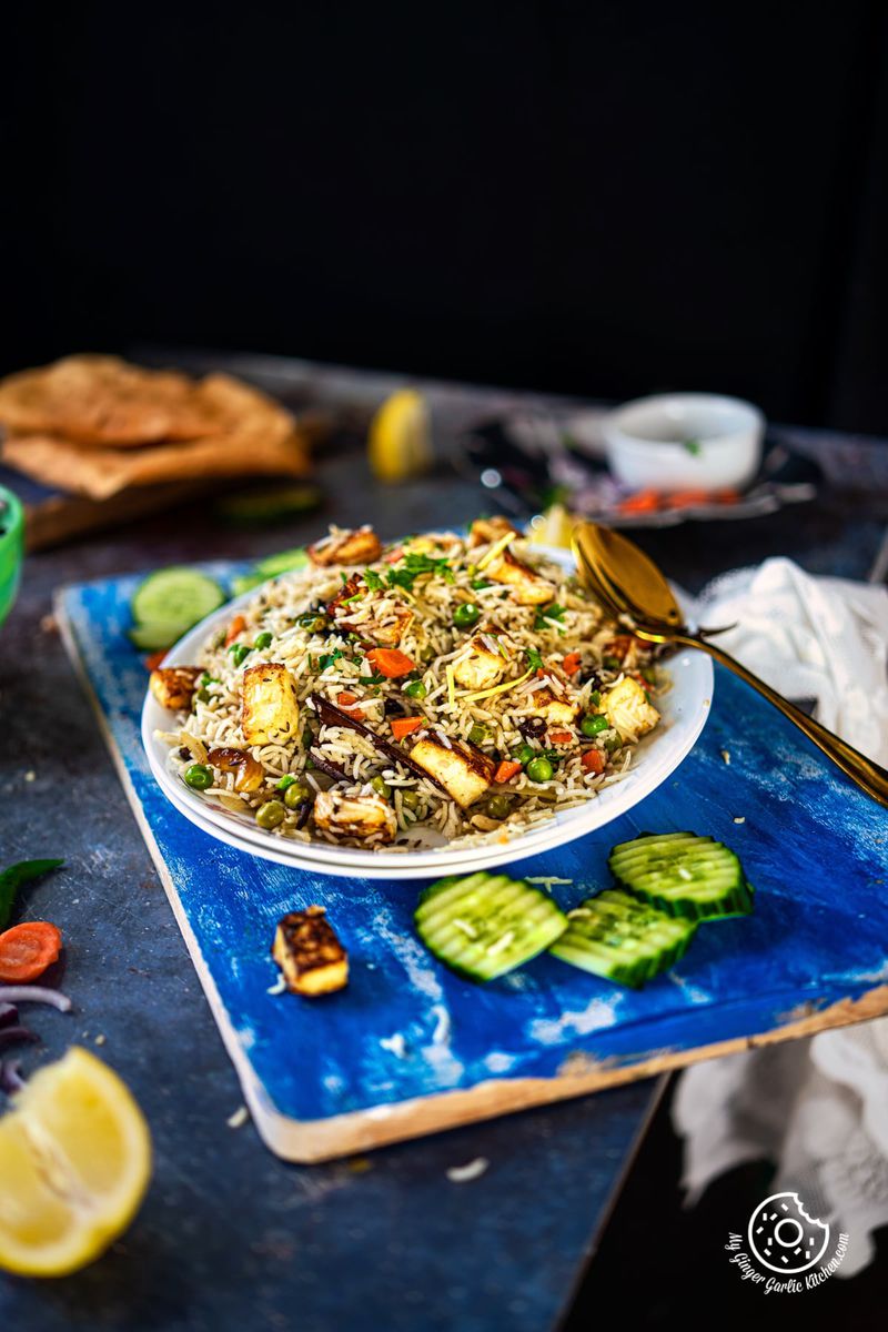 paneer pulao (paneer rice)served on a white plate with cucumber on the side