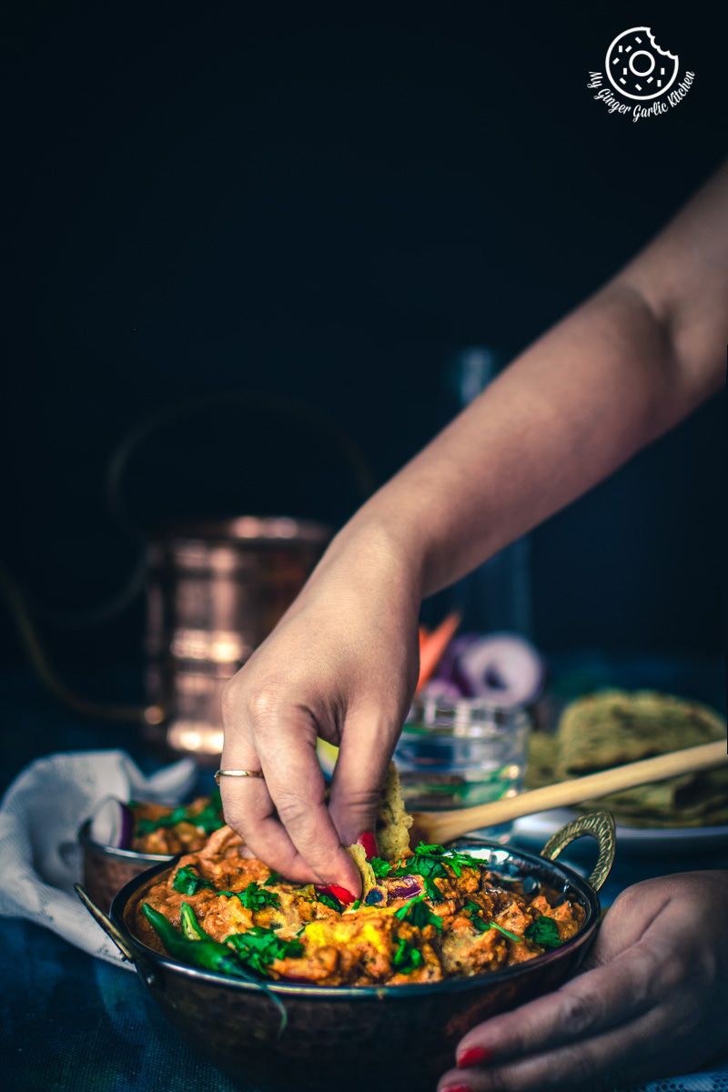 someone is taking a bite of paneer tikka masala from a copper bowl on a table