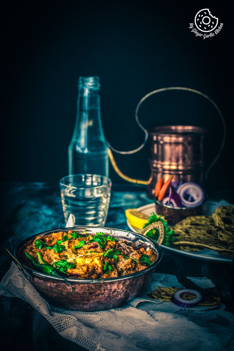 a bowl of paneer tikka masala on a table with a bottle of water
