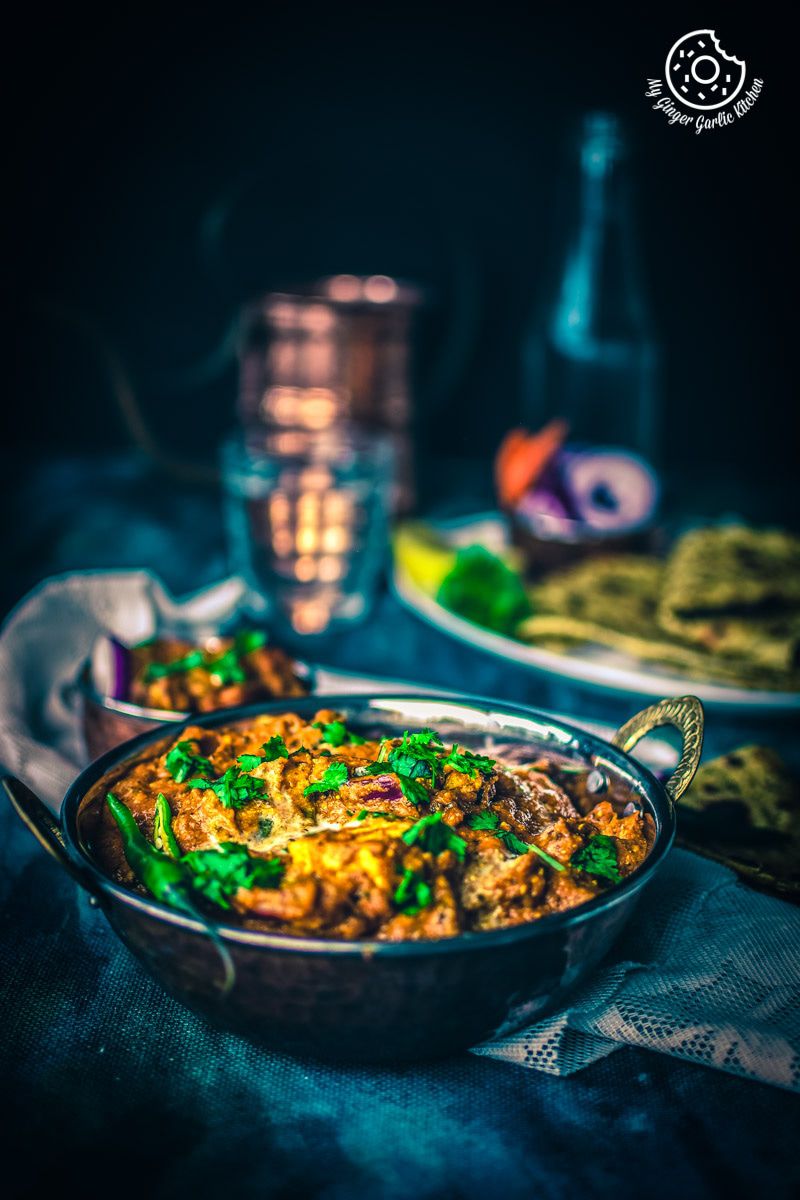 a bowl of paneer tikka masala on a table with a glass of water in background