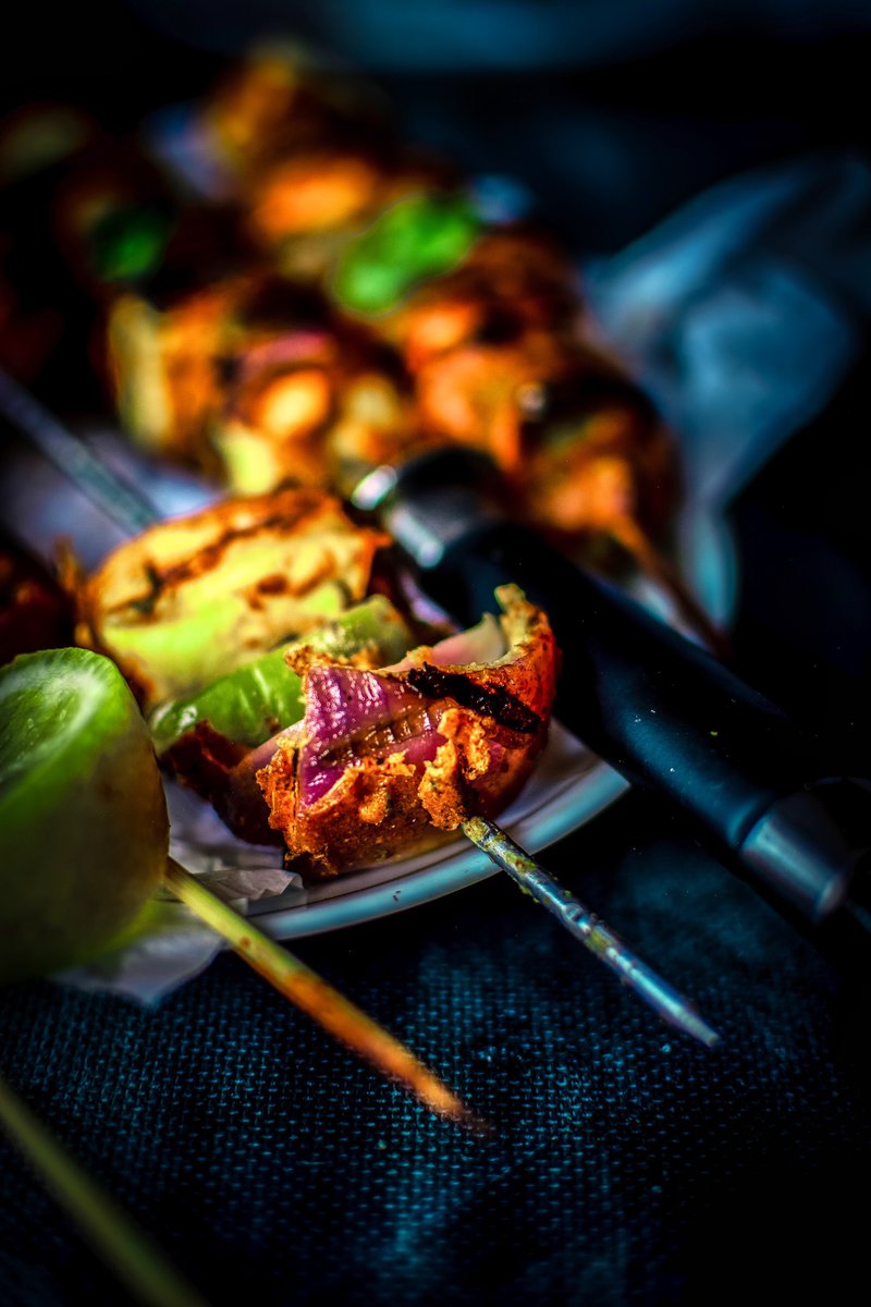 Dramatic close-up of a skewers of paneer tikka with a bokeh effect, emphasizing the textures and colors.