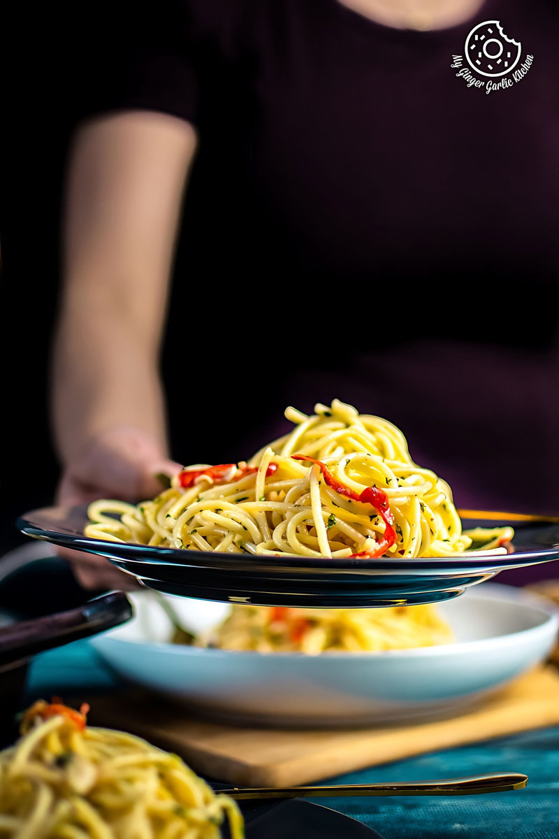 a female holding pasta aglio e olio served in a grey plate