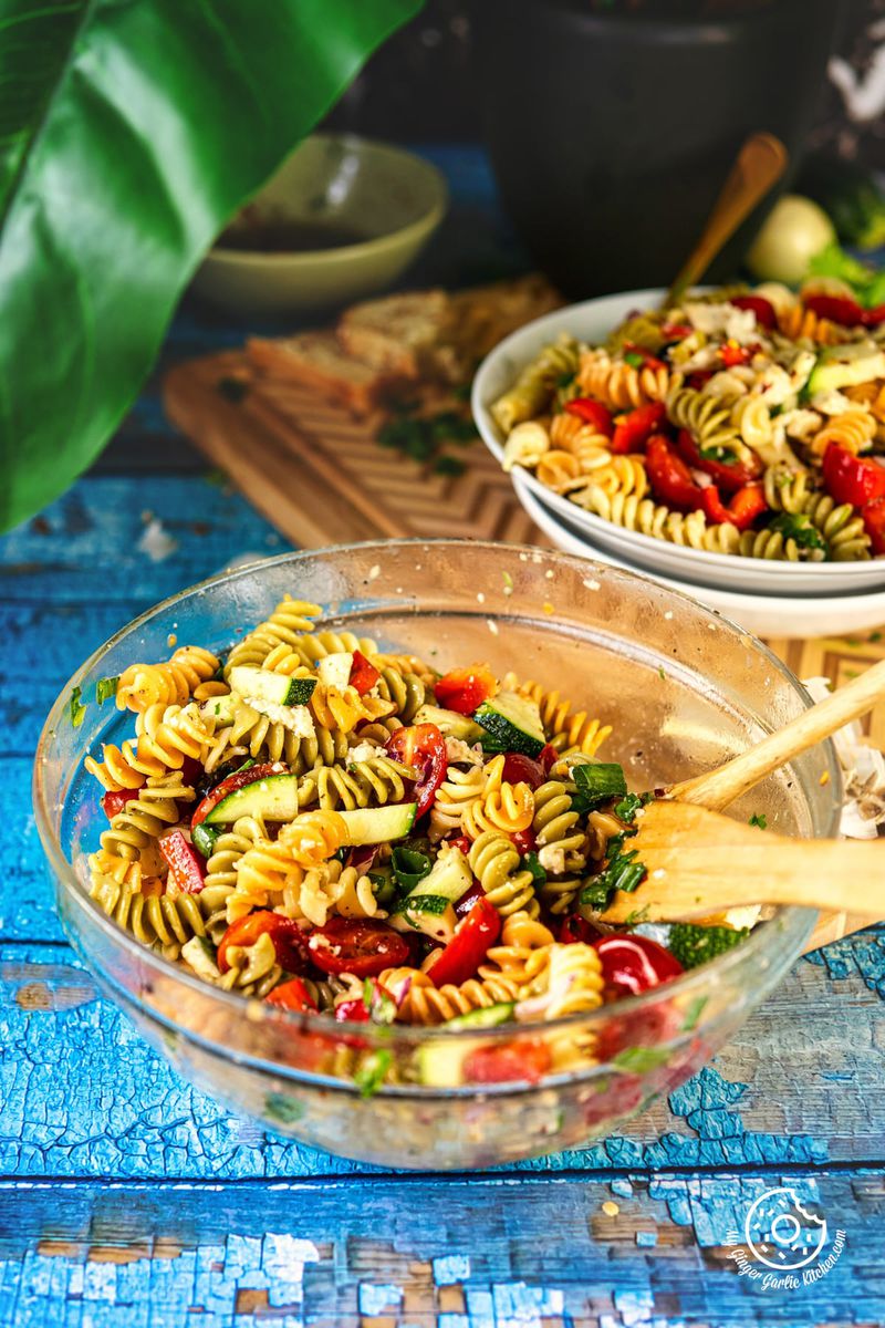 there are two bowls of pasta salad with wooden spoons on a table