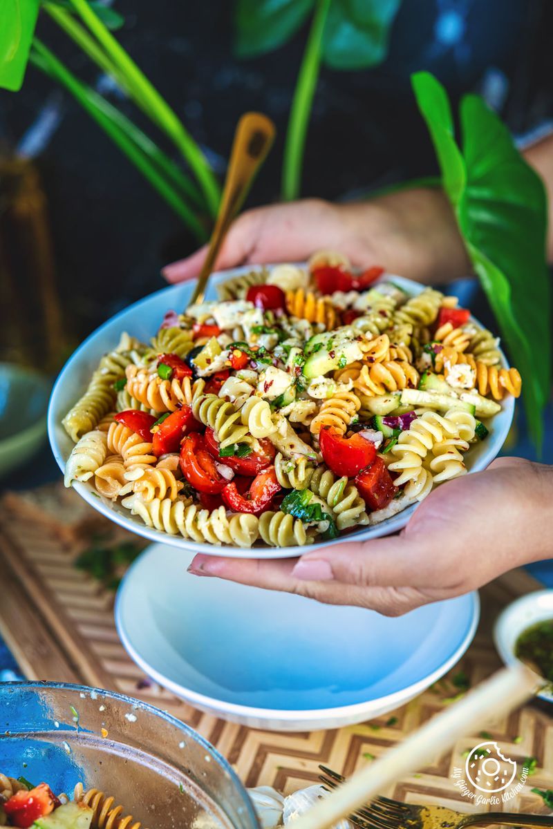 photo of a person holding a plate of pasta with a bowl of salad in the background