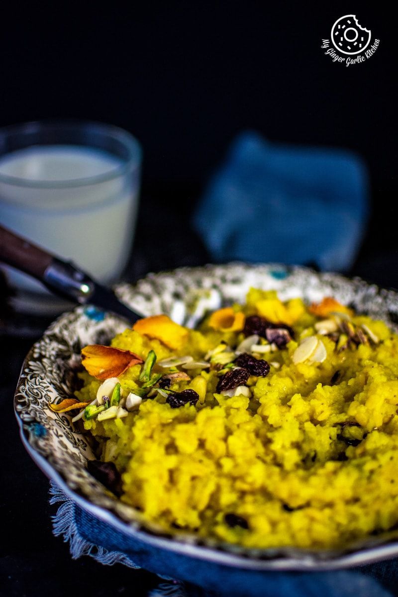 a plate of jaipuri paush khichda aka sweet dal khichdi with a spoon and a glass of milk in background