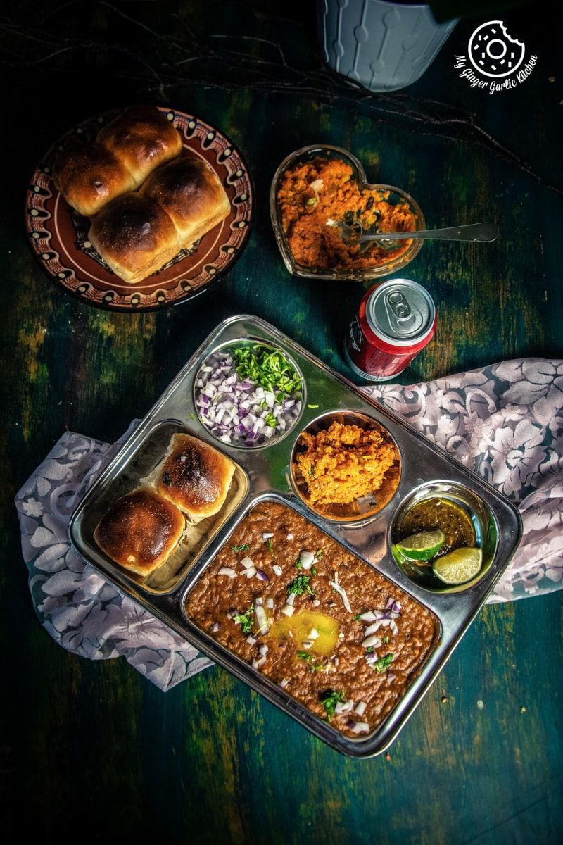 pav bhaji with onions, and halwas in a tray on a table with more pavs and gajar halwa on the side