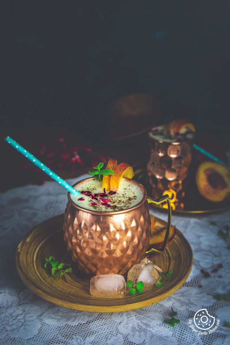 peach lassi decorated with dried rose petals served in a copper mug