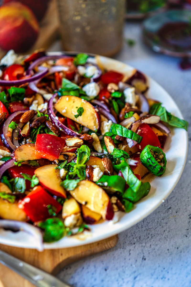 Artfully arranged peach salad with sliced peaches, red onions, bell peppers, fresh herbs, and nuts on a white plate, perfect for a healthy meal.