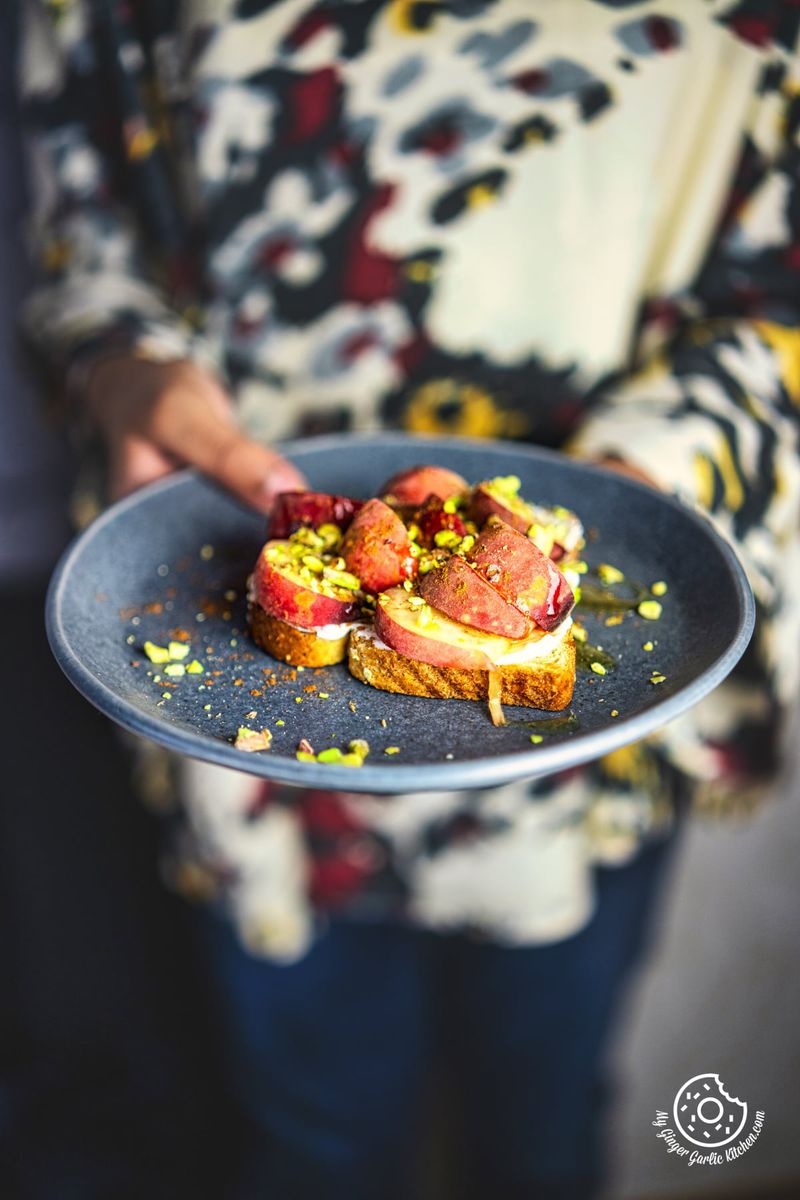 photo of a person holding a plate with a peach toast and nuts on it