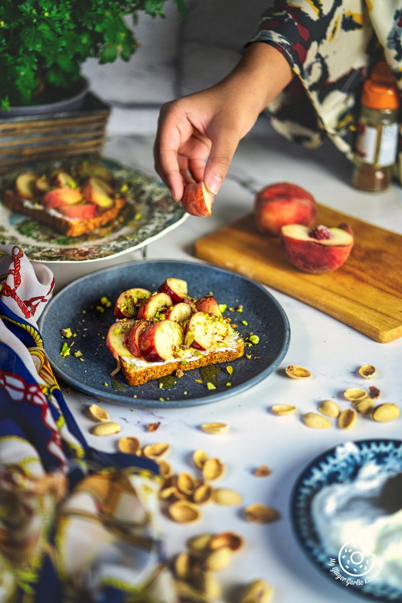 photo of a person is putting a piece of peach on a the peach toast