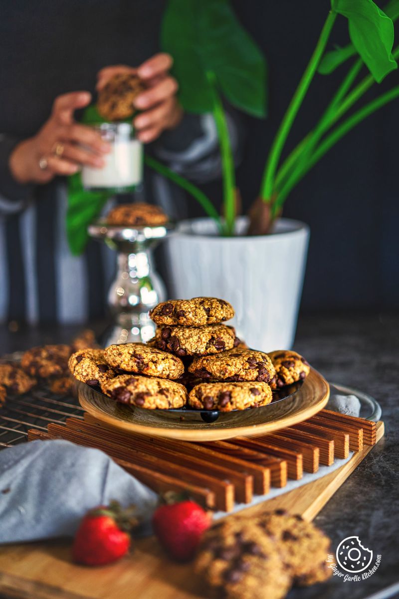 peanut butter banana oatmeal cookies in a plate and a female holding a glass of milk in the background