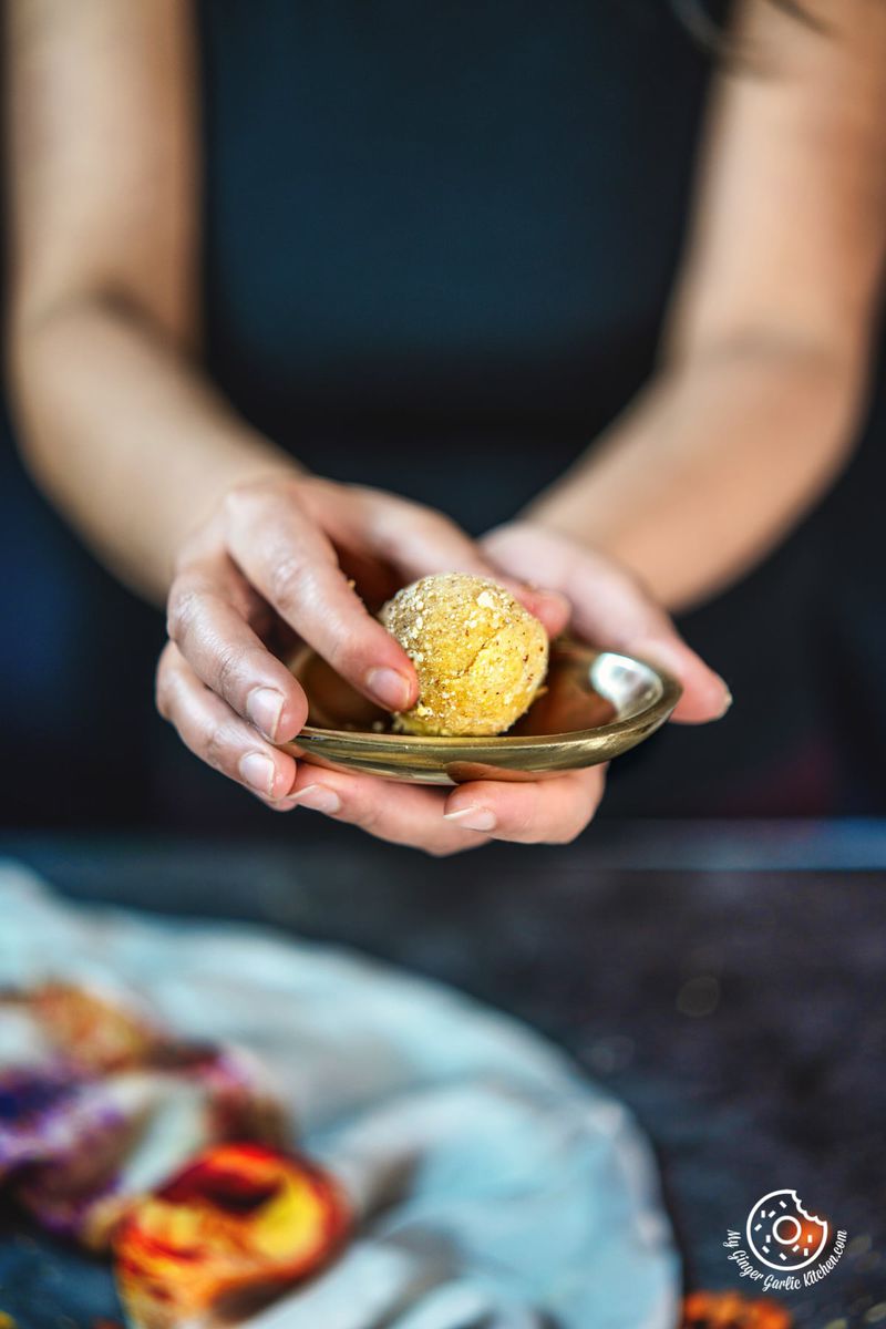 a female holding a peanut ladoo in one hand and a golden plate other hand
