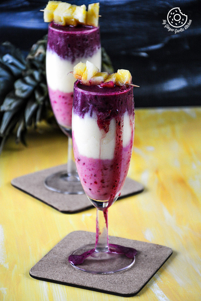 two glasses of pineapple blueberry raspberry breakfast layered smoothie on a table
