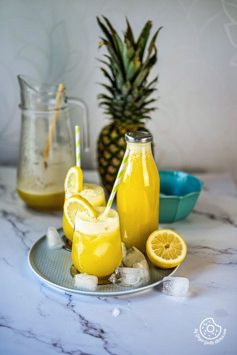 two pineapple juice glasses in a plate with half lemon and ice cubes