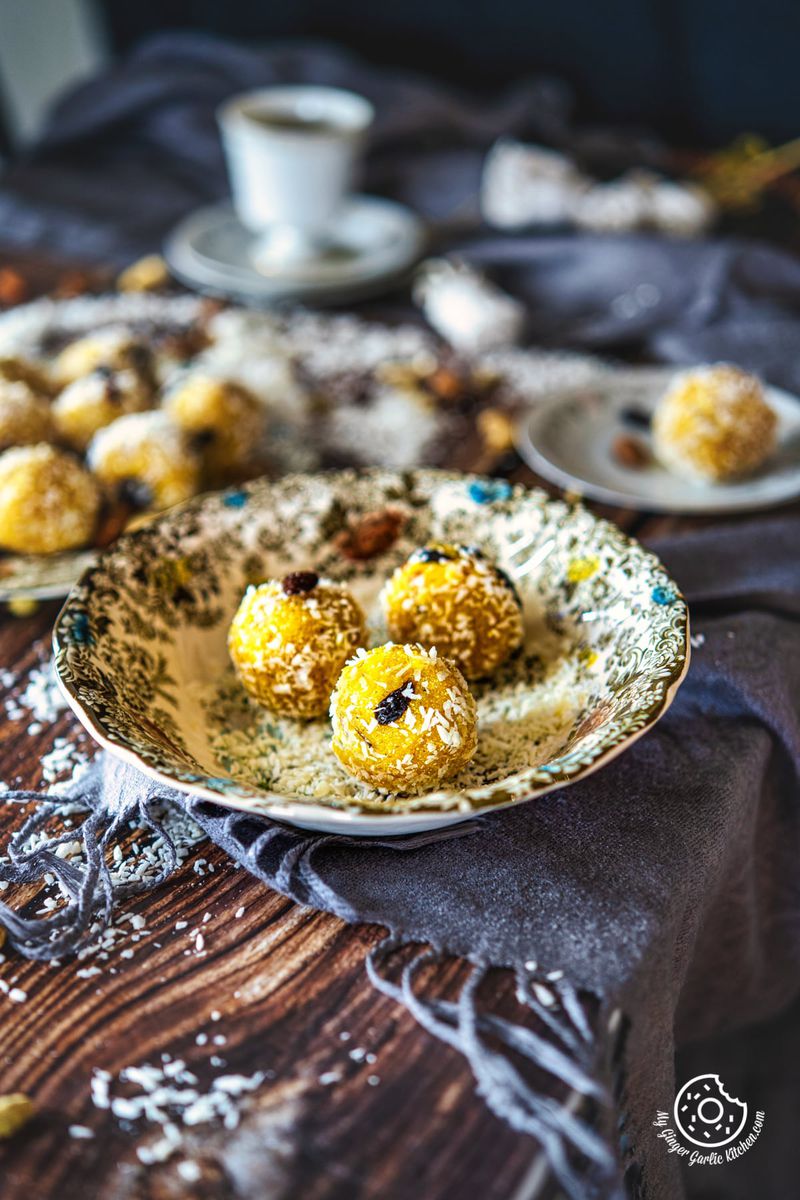 three pineapple ladoos in a floral plate with more ladoos and a tea cup in the background