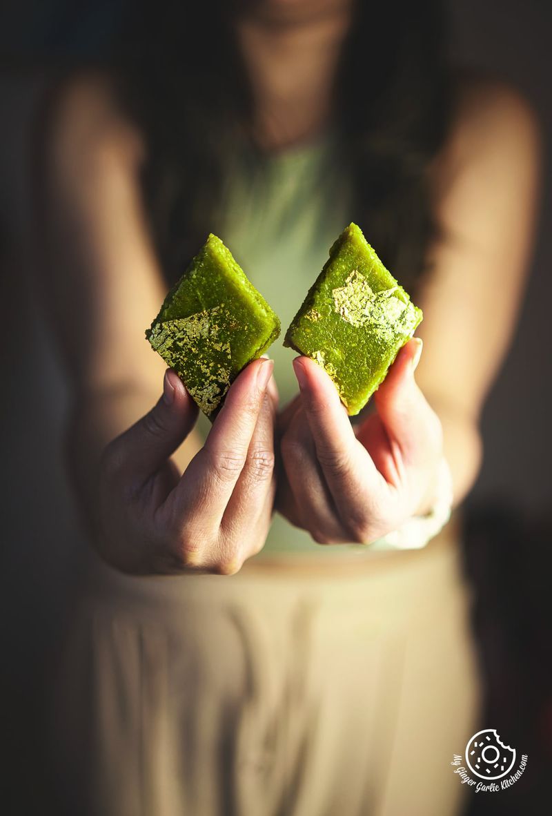 closeup of a female holding two golden leaves garnished pista katli pieces