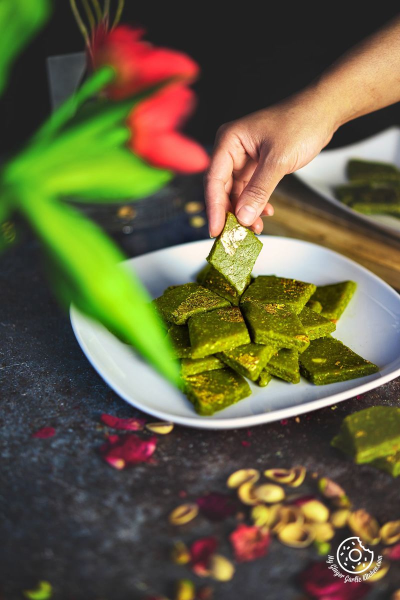 a hand holding a pista katli over a stack of pista katlis