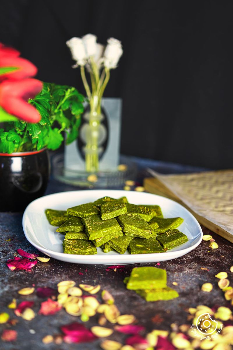 a stack of pista katli arranged on a white plate with two pista katlis and rose petals on the side