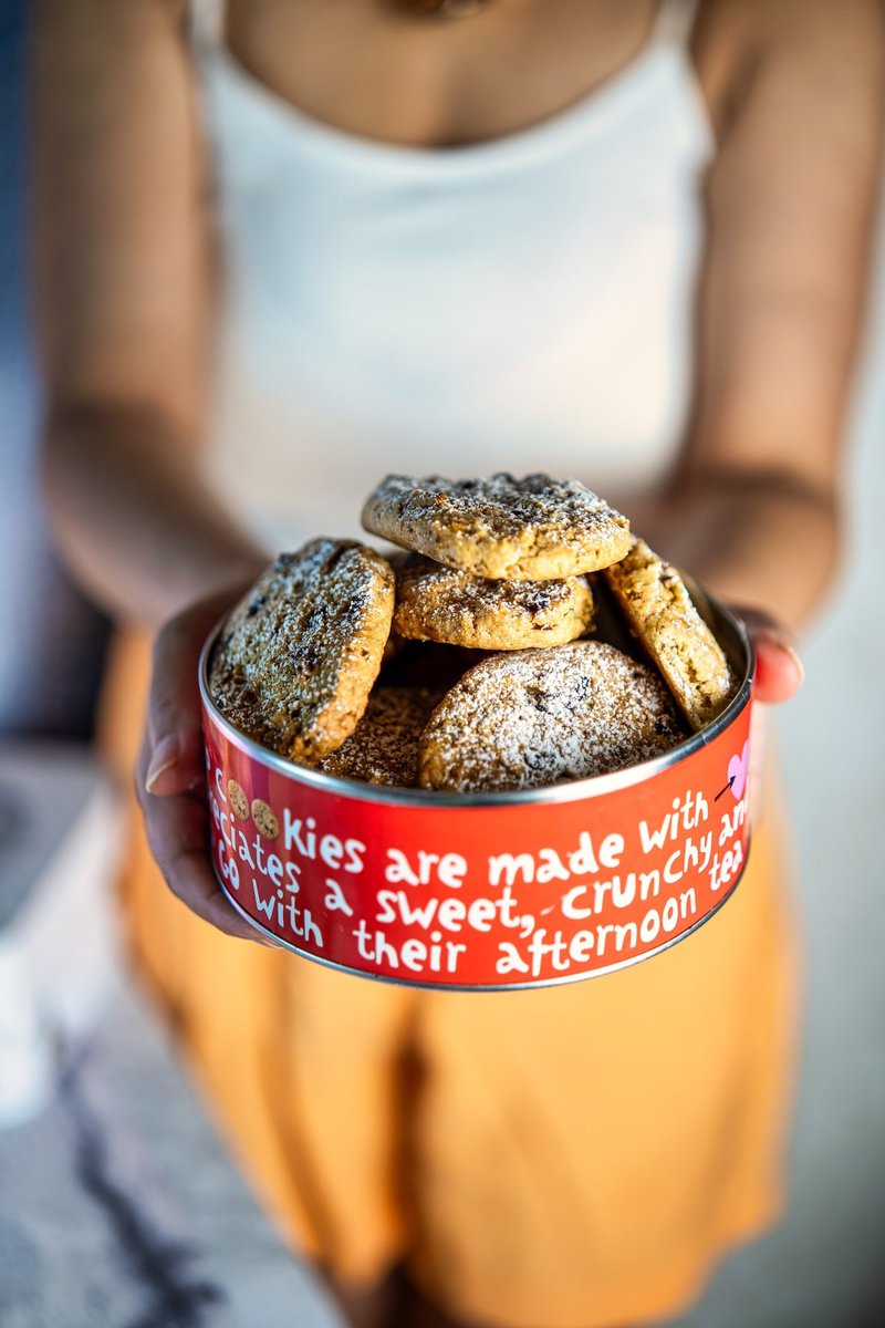 A person's hands holding a tin filled with pistachio cranberry cookies, with the same text overlay as the previous image.