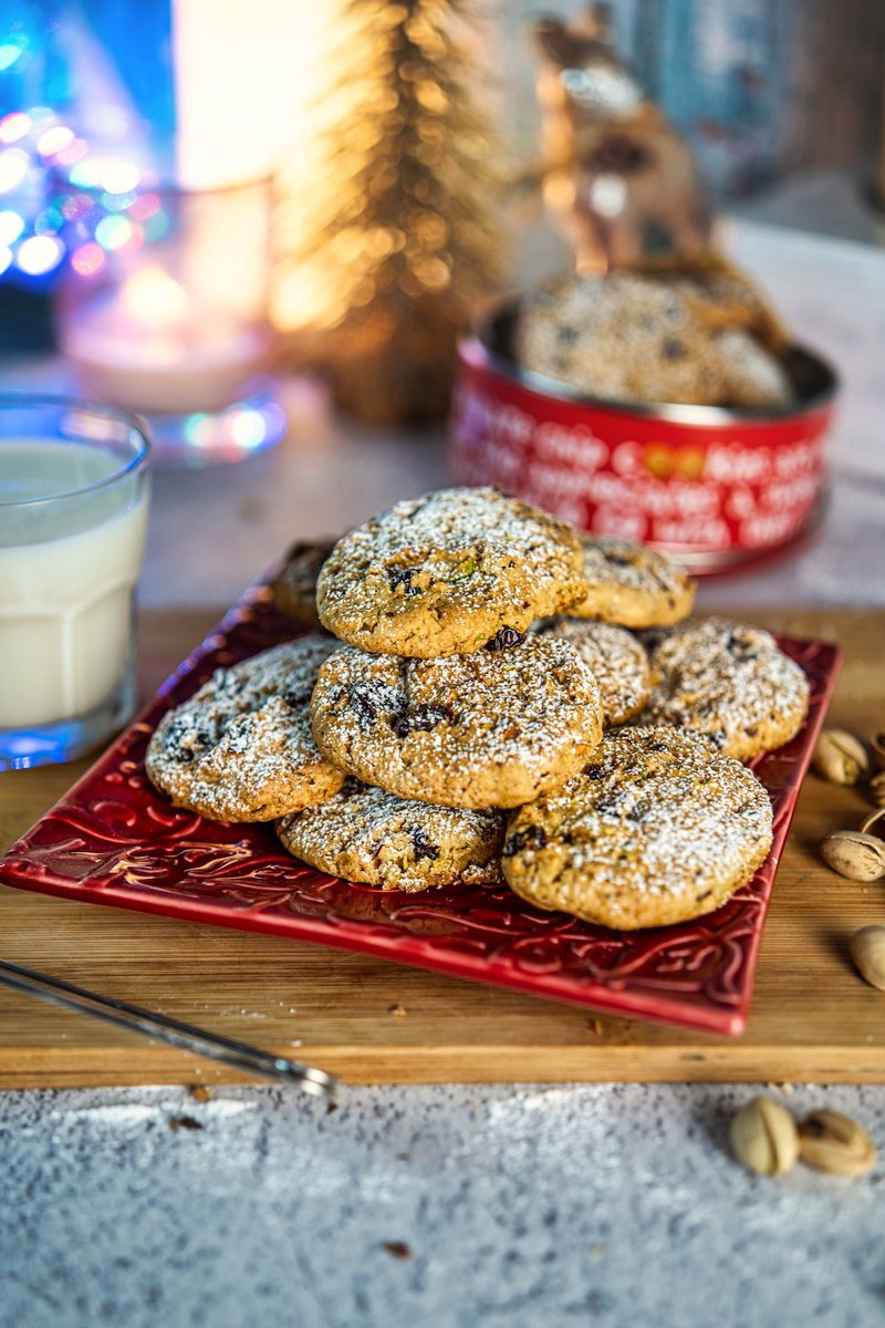 A close-up of pistachio cranberry cookies in a decorative tin with a text overlay mentioning that the cookies are made with a sweet, crunchy ingredient.