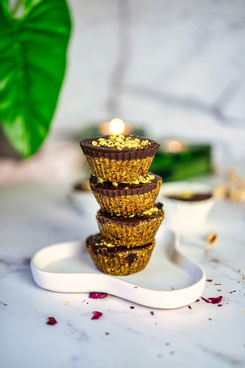 Stack of pistachio date cups with chocolate topping on a modern white plate, decorative green leaf in the background.