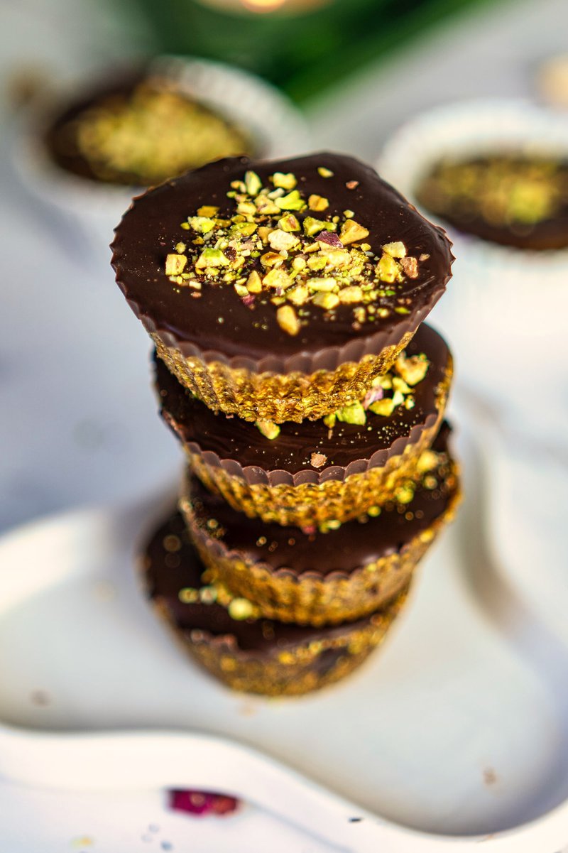 Close-up of stacked pistachio date cups garnished with chopped pistachios on a sleek white spoon.