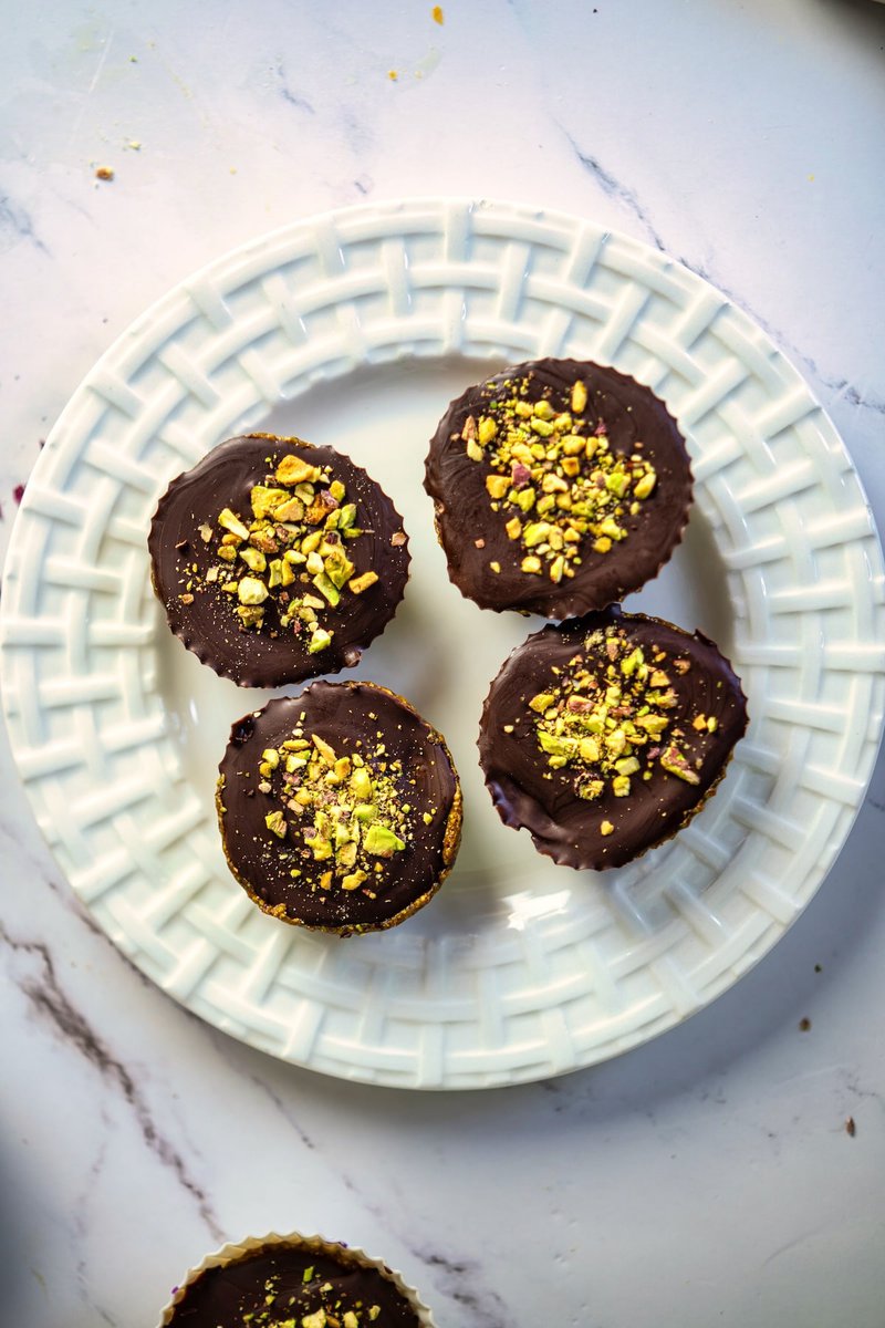 Beautiful presentation of pistachio date cups on a white lattice-patterned plate, sprinkled with crushed pistachios.