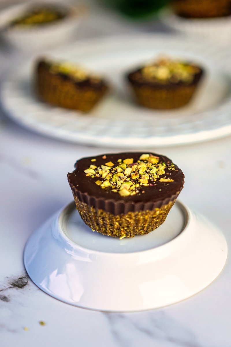 Single pistachio date cup on a small white ceramic dish, beautifully topped with crushed pistachios.