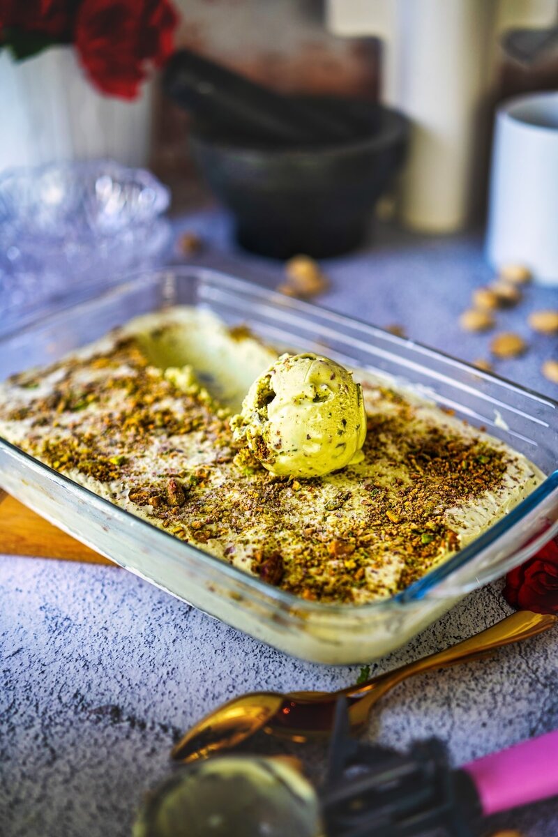 Homemade pistachio ice cream in a glass dish, topped with crushed pistachios and a single scoop, easy pistachio ice cream recipe