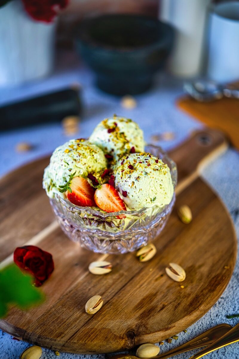 Overhead view of rich pistachio ice cream scoops topped with fresh strawberry slices and crushed pistachios in crystal dessert bowl - no-churn ice cream recipe
