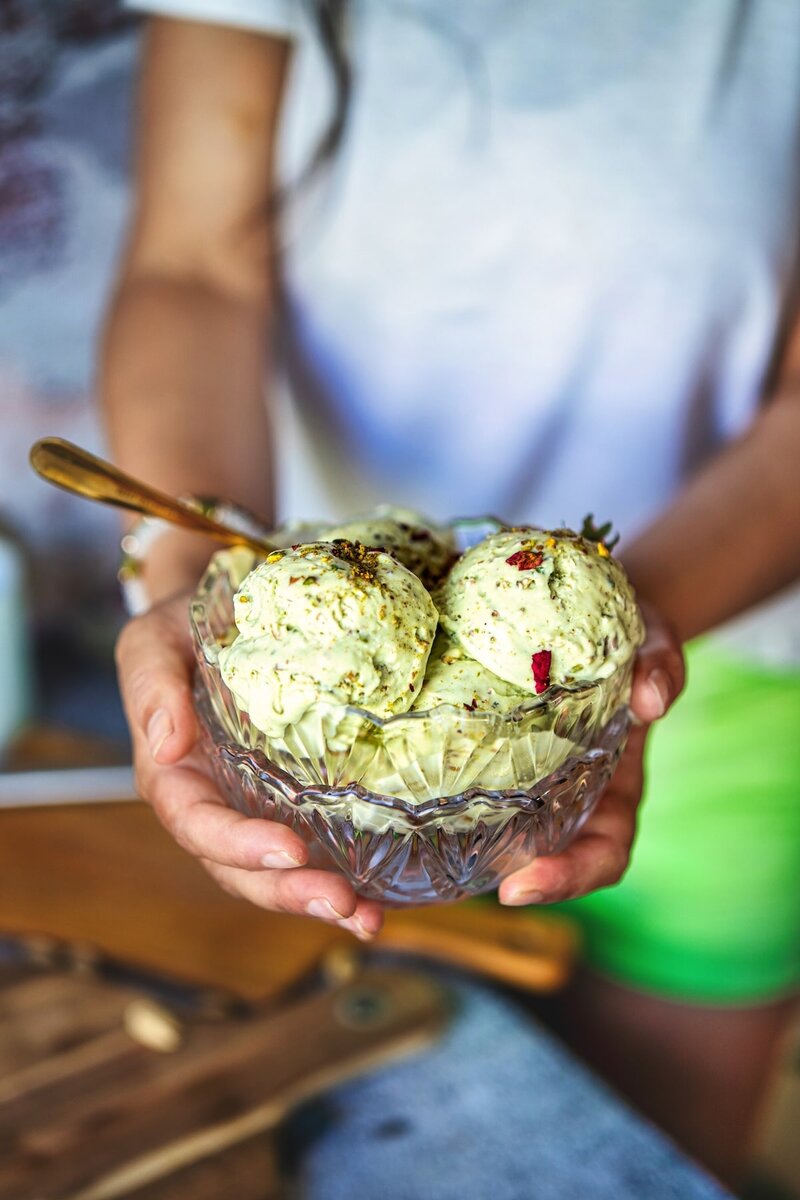 Creamy pistachio ice cream scoops served in crystal bowl with fresh strawberries and crushed pistachios on wooden serving board - healthy gourmet dessert