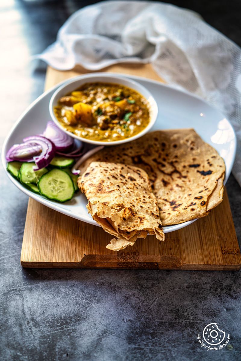 photo of a plate of plain paratha with a bowl of curry and salads