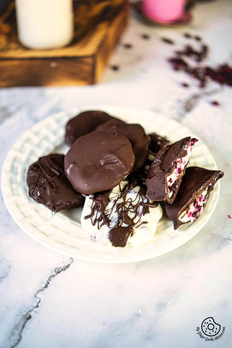 a plate with chocolate covered pomegranate greek yogurt bites and a candle next to it 