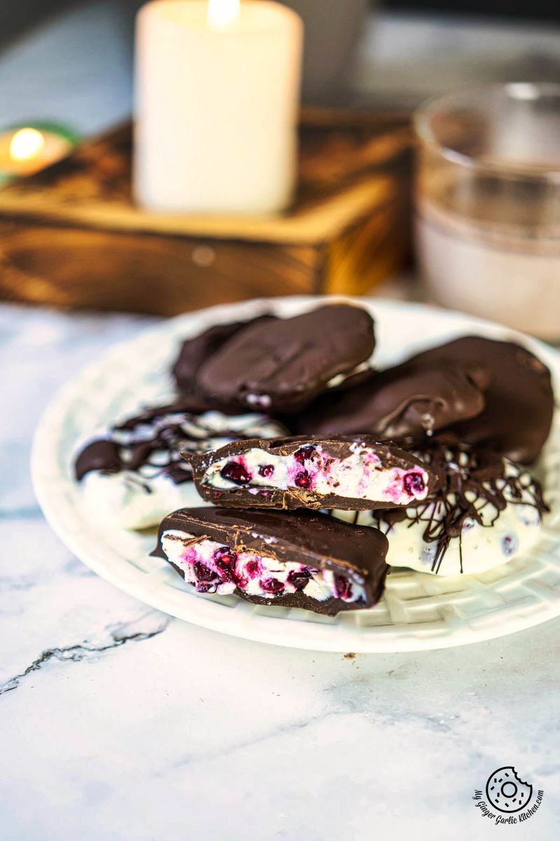 a plate filled with chocolate covered pomegranate greek yogurt bites next to pink and white candles in the background