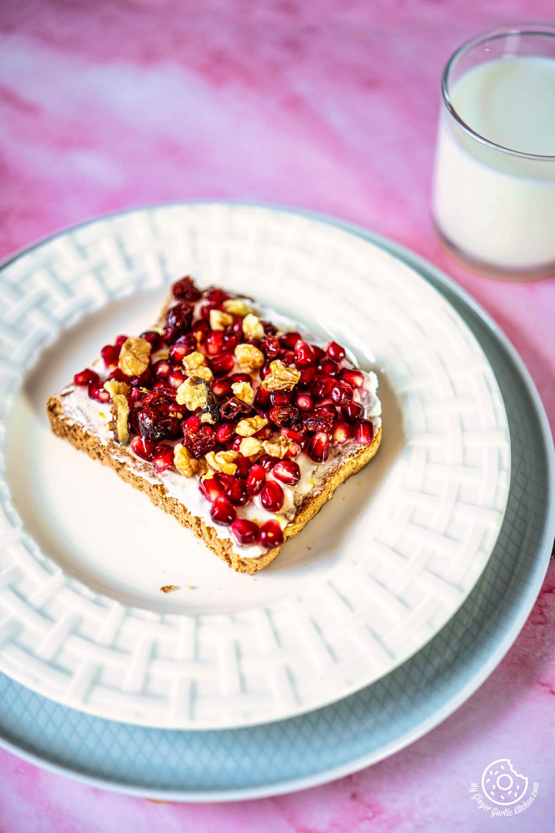 a piece of pomegranate toast with fruit on a plate next to a glass of milk