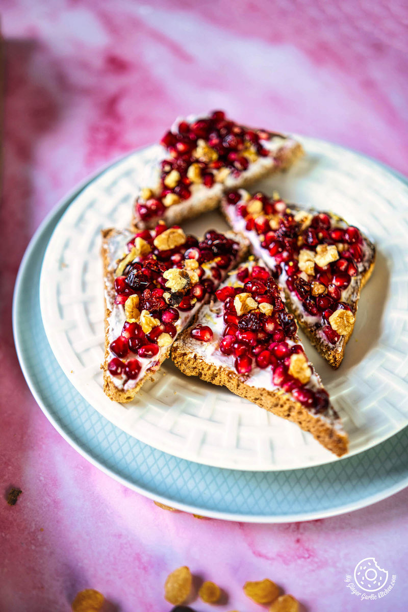 four pieces of pomegranate toast on a plate with nuts and cranberries