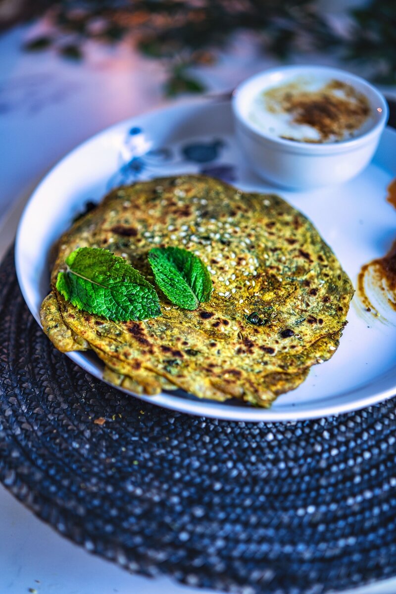 Mint paratha garnished with fresh mint leaves on a white plate, served with a bowl of yogurt.