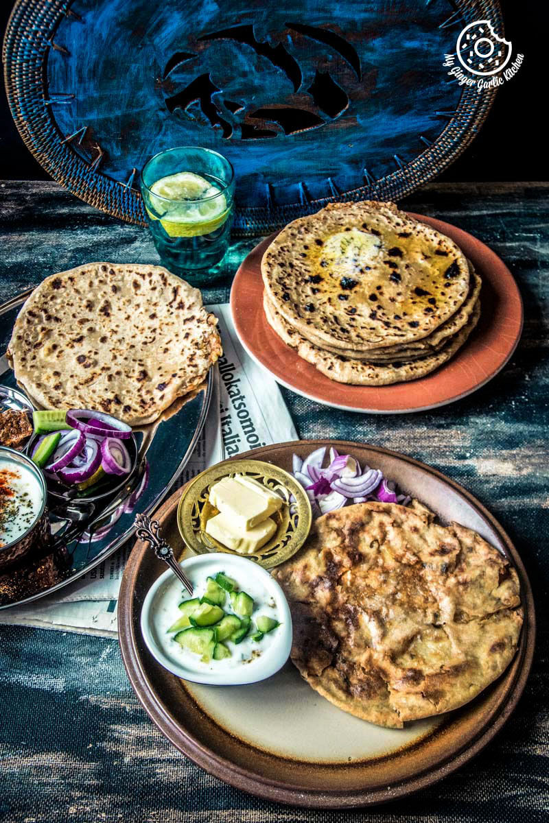 there are three plates of tandoori aloo ka paratha and punjabi aloo paratha on a table with a glass of water