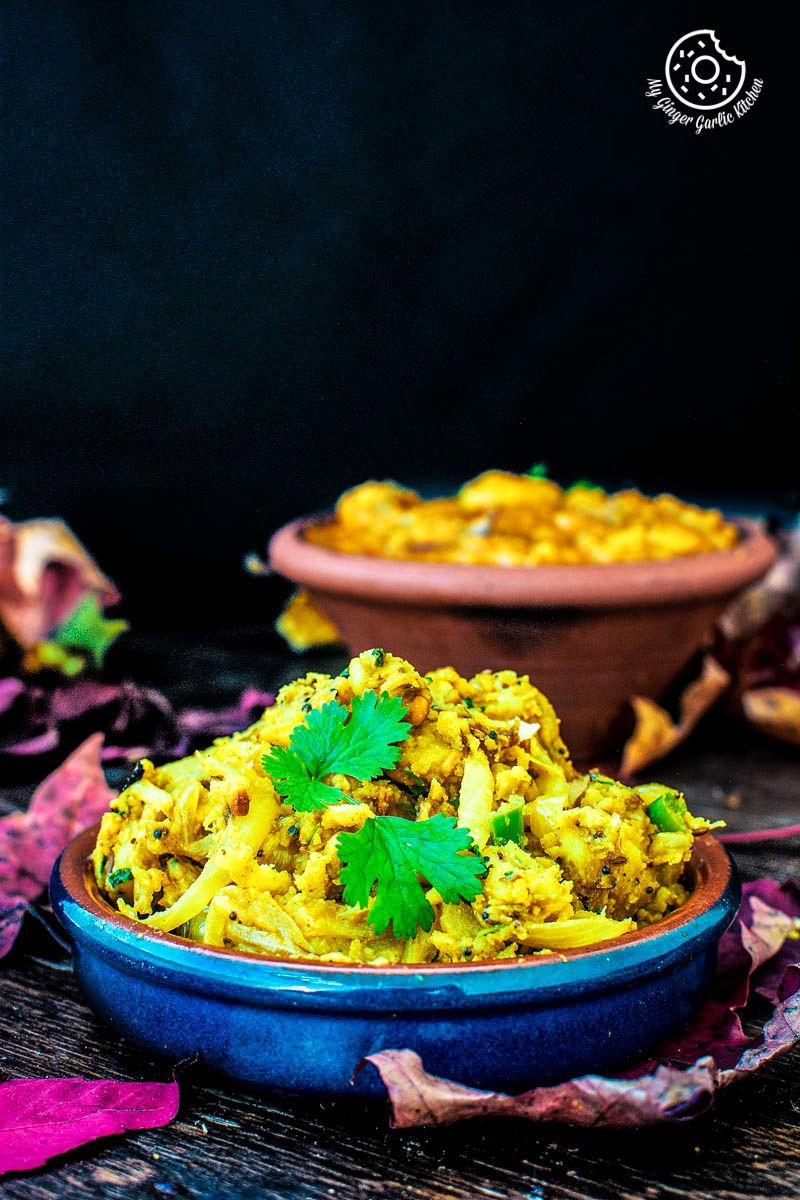 a bowl of aloo bhaji with some leaves with a bowl of sabji in backround