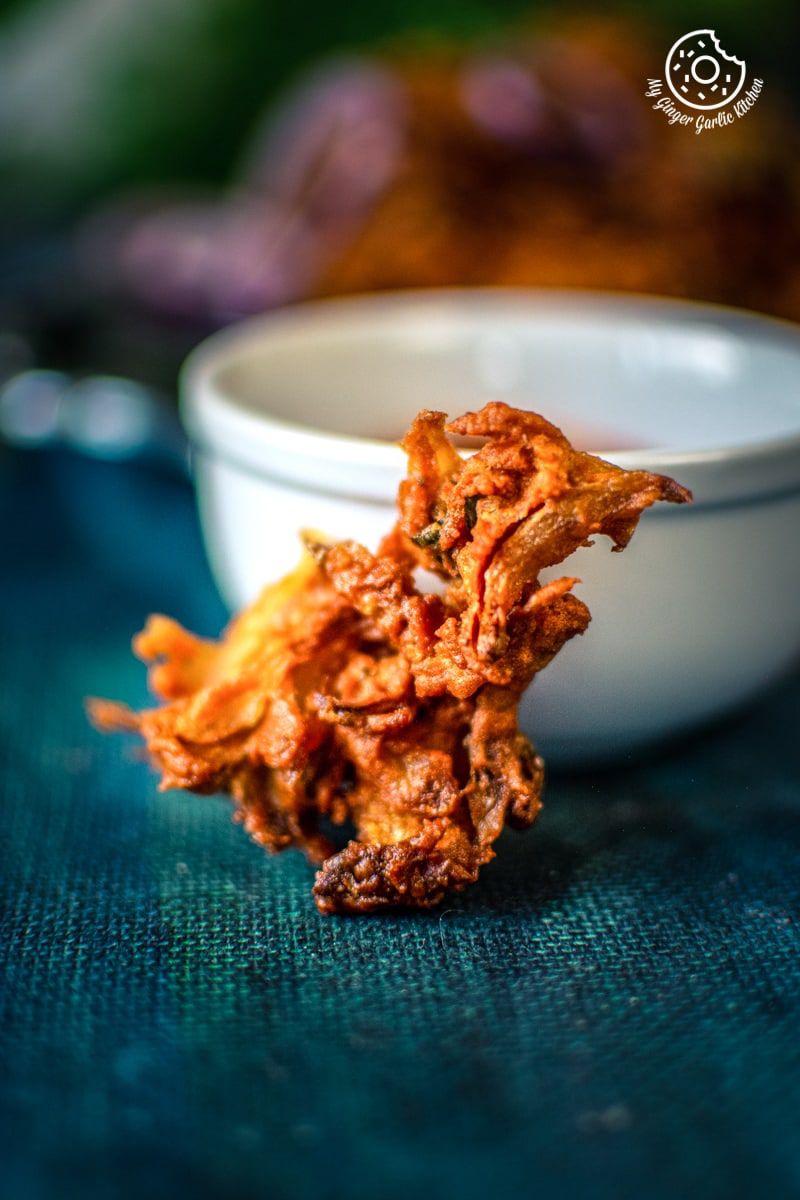 onion pakoda on the blueish background and a white bowl in the background