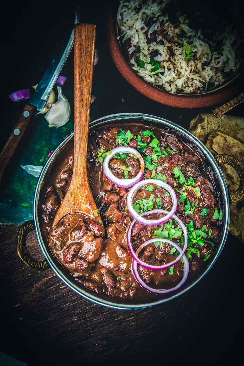 A photo of a bowl of rajma masala, a popular North Indian dish made with red kidney beans in a gravy. The dish is garnished with cilantro and onion rings.