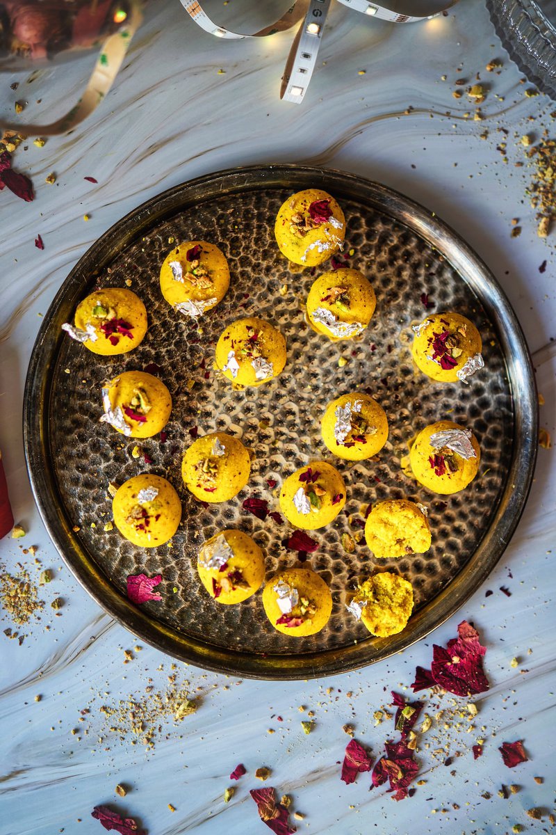 A tray of Rasmalai Ladoo topped with edible silver leaf and garnished with dried rose petals.