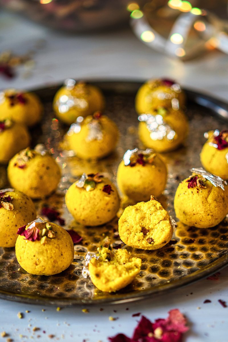 Plate of Rasmalai Ladoo garnished with pistachios, rose petals, and edible silver foil, displayed on a textured platter.