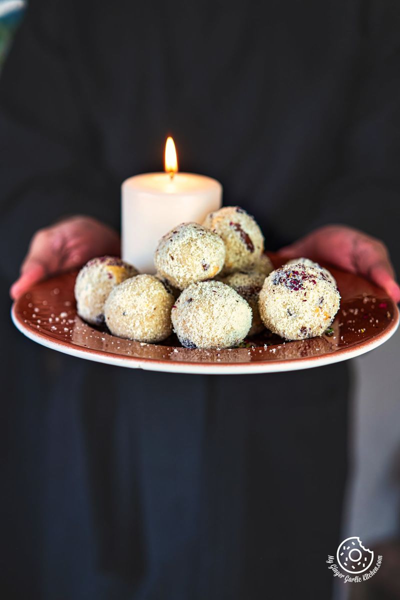 photo of a person holding a plate of rava ladoos with a candle