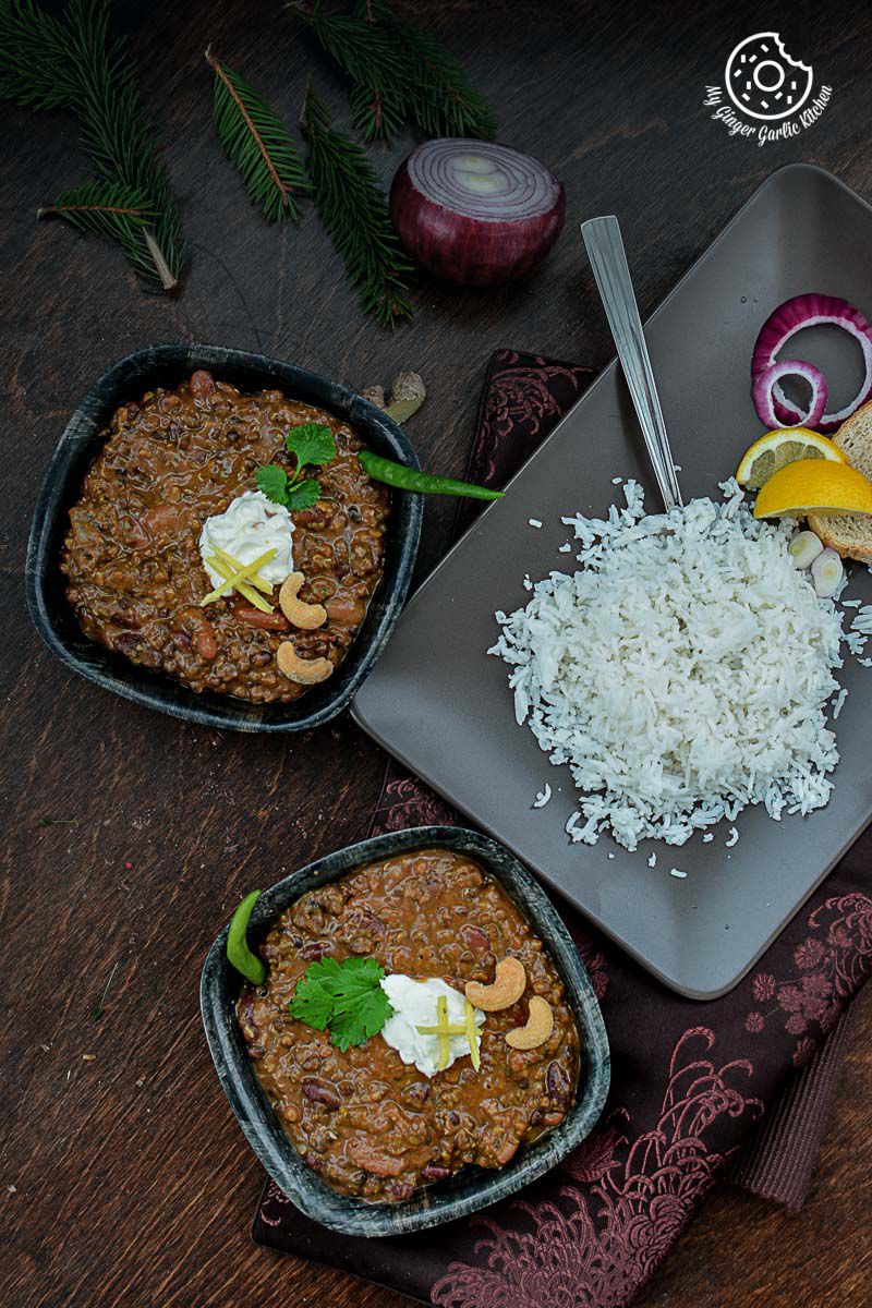 two bowls of three bean thick dal makhani on a table with rice and vegetables
