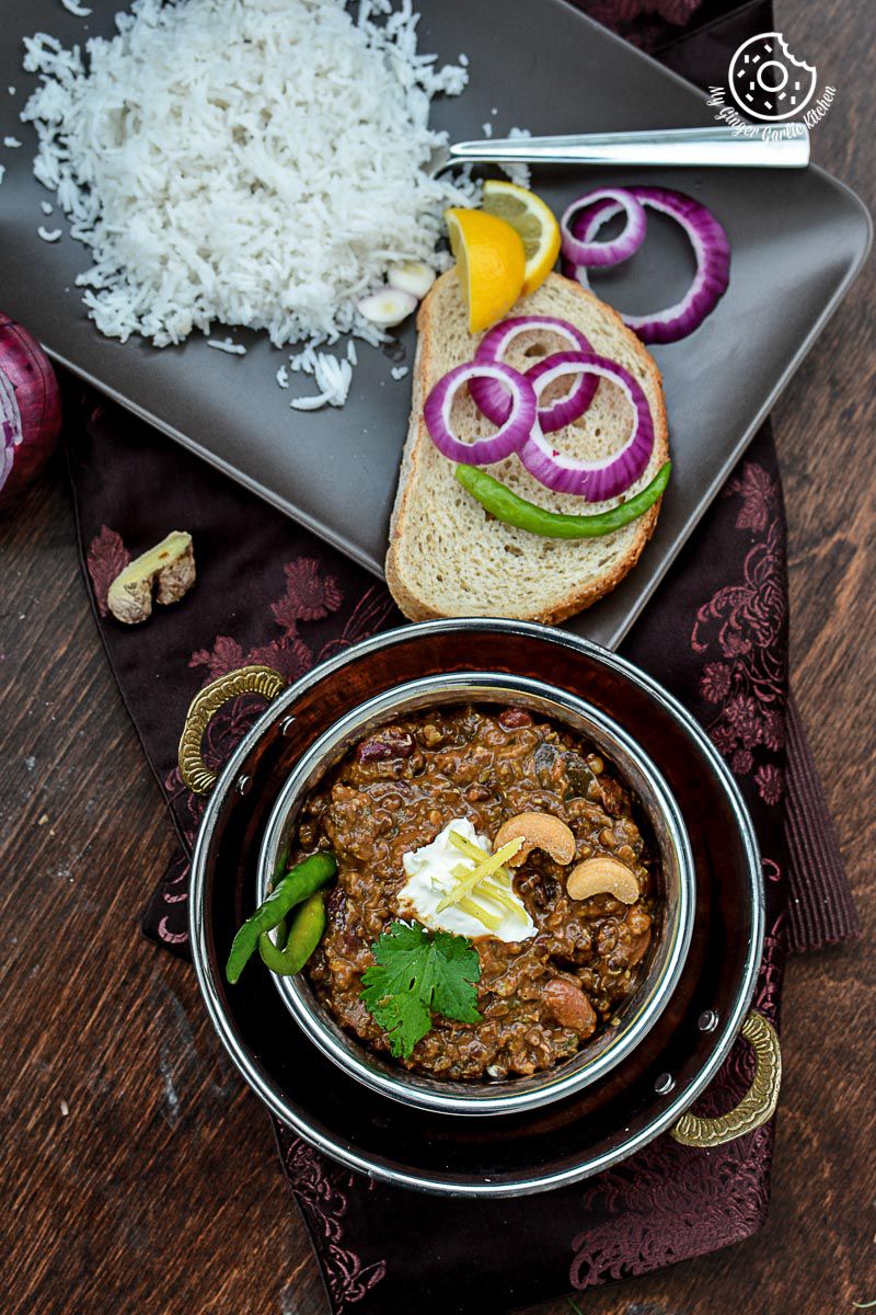 a bowl of three bean thick dal makhani with bread and rice on a table