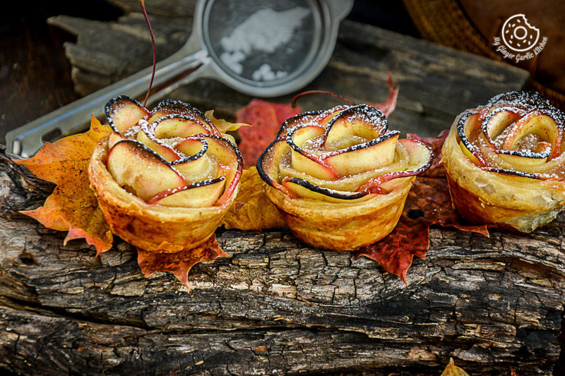 three apple rose mini tartlets on a log with leaves and a measuring spoon