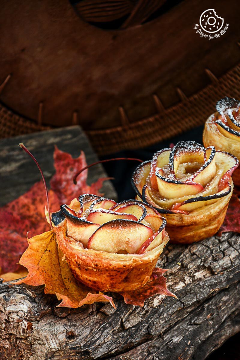 three apple rose mini tartlets pastries on a log with leaves on it